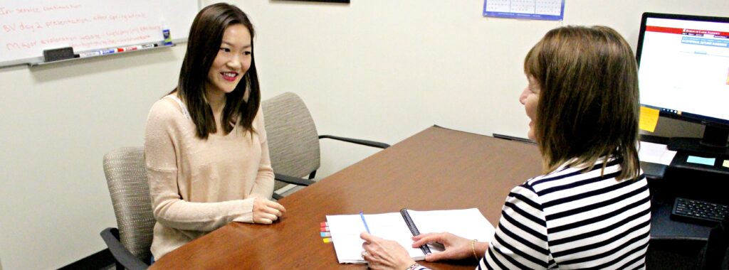 An advisor and student at table reviewing a planner.