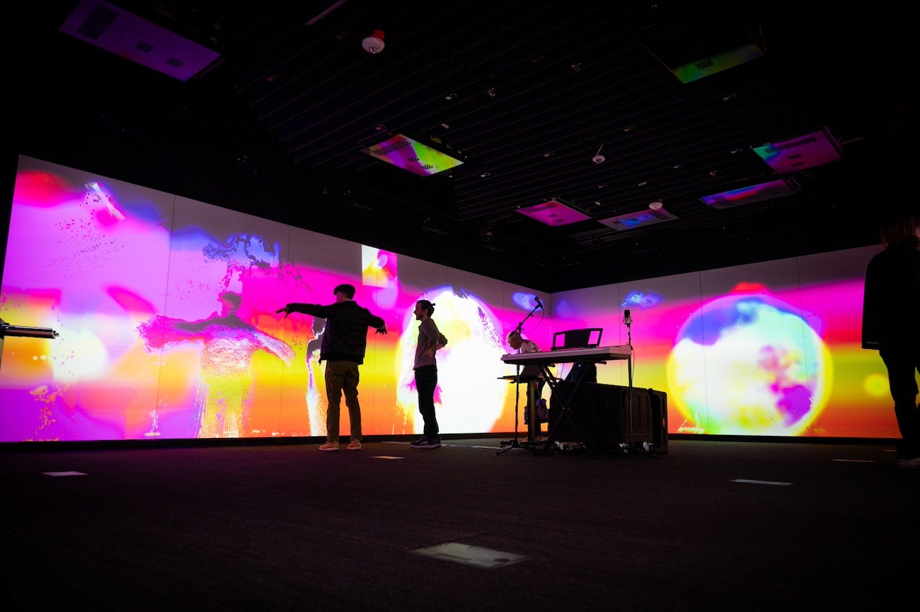 Two persons stand in front of a colorful video wall in an interactive art exhibit