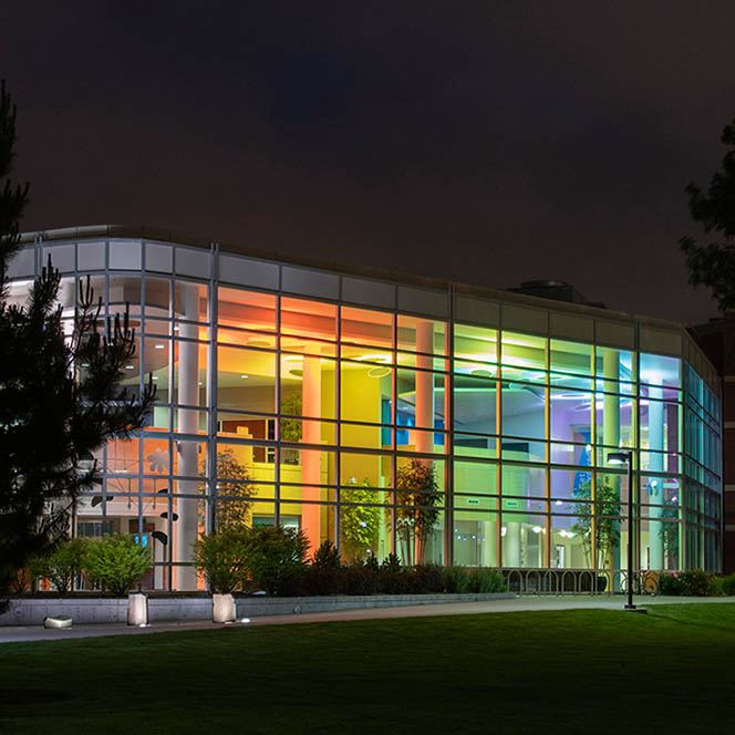 Glass-faced atrium of the Student Union Building, lit with colorful lights against a dark night sky.