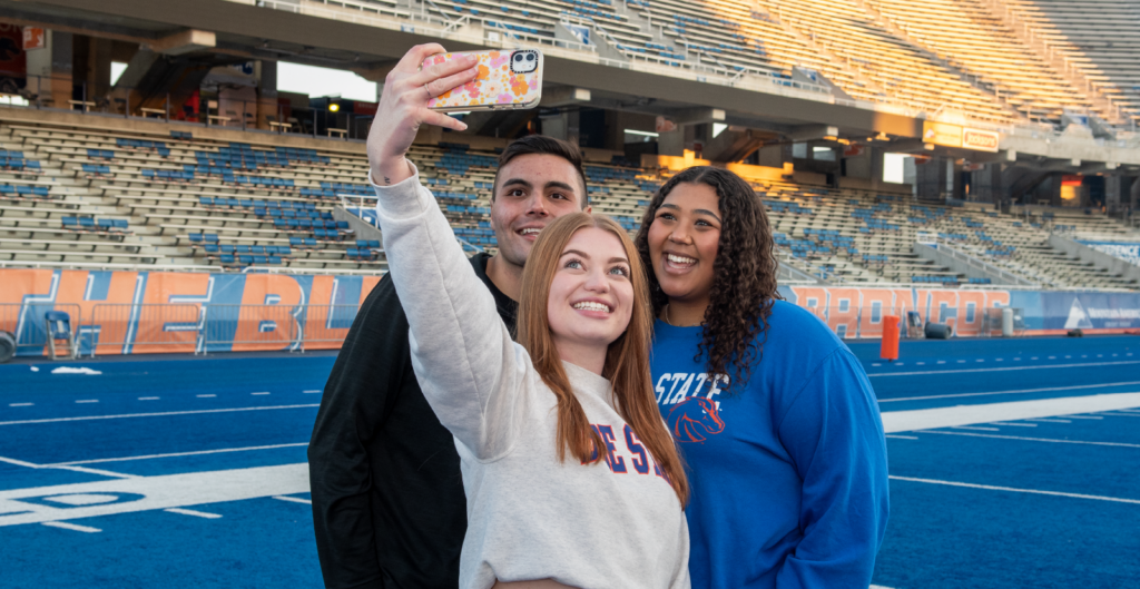 Boise State students gathering on the blue turf to take a selfie.