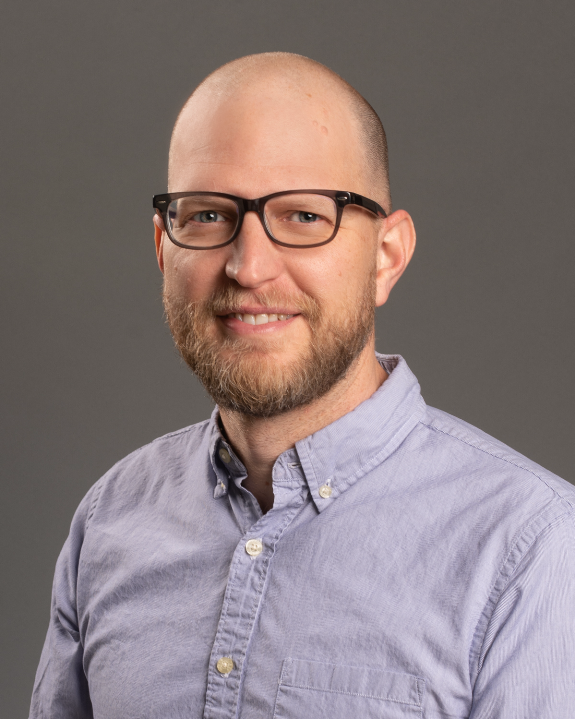 Man with blue shirt, balding, wearing glasses