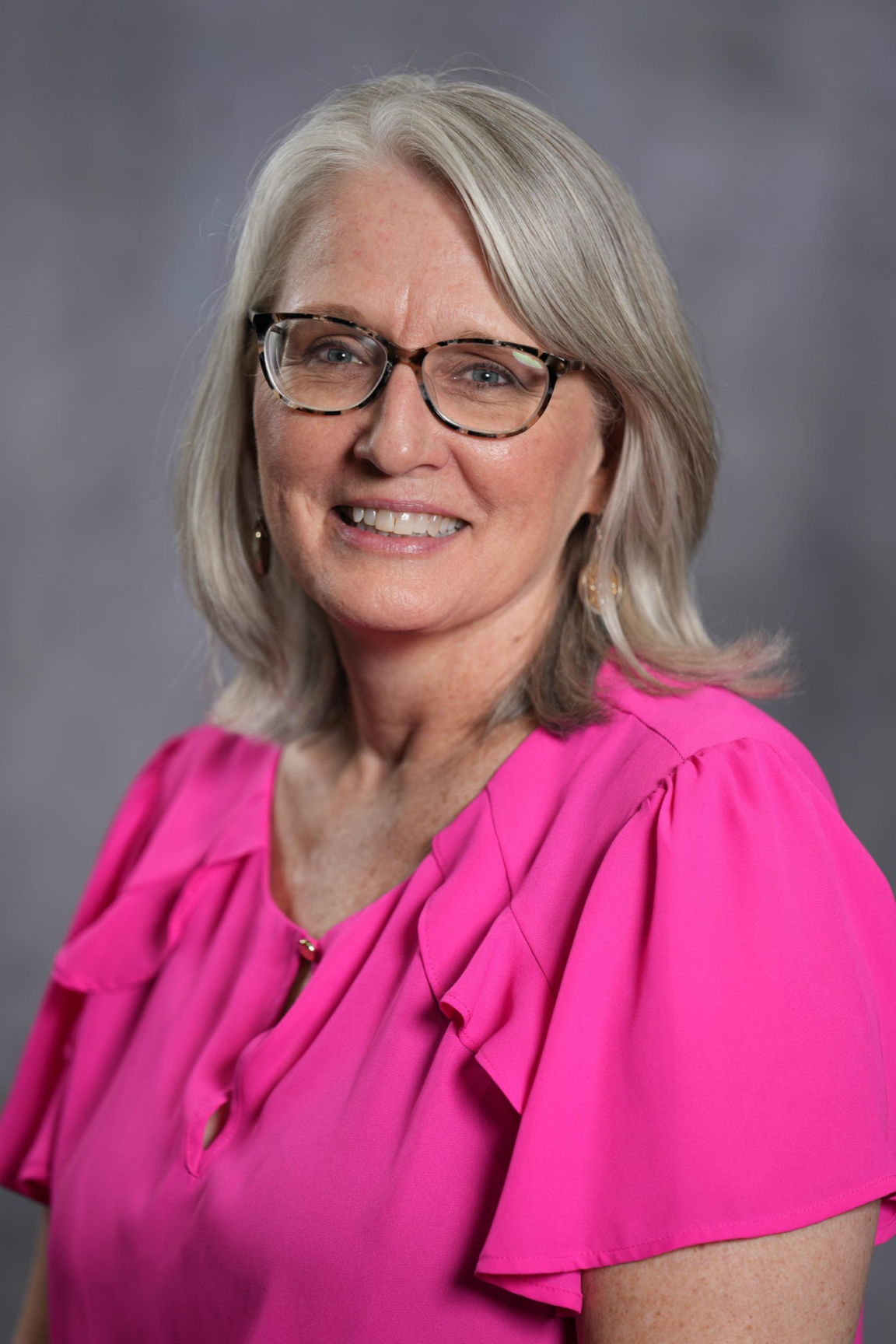 Woman with a pink shirt, grey hair, and glasses.