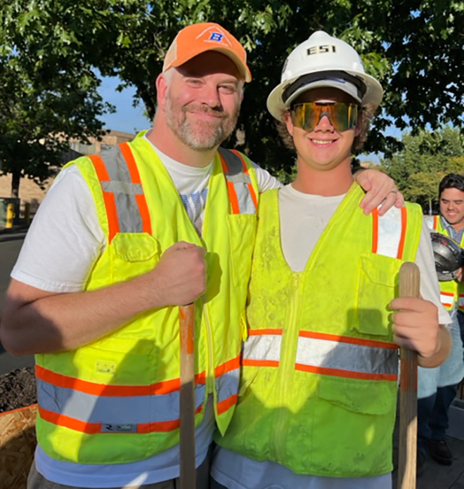 father and son wearing reflective vests, holding shovels