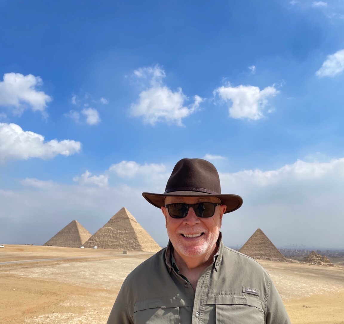 Tom wearing a hat and sunglasses stands in front of pyramids