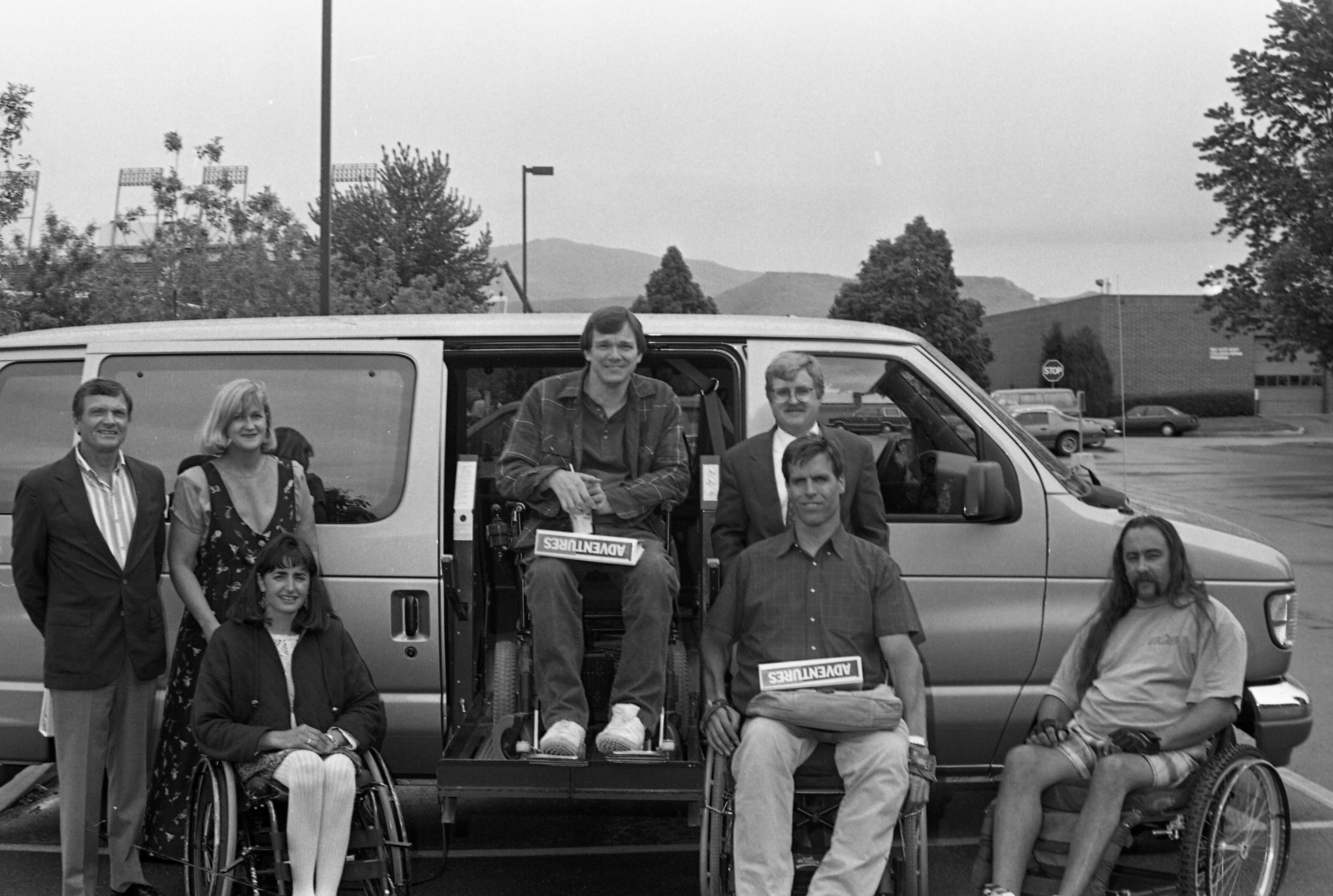 Group of people, some in wheelchairs, pose in front of a van with a wheelchair lift
