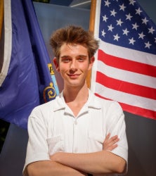 Student standing in front of flags with arms crossed smiling