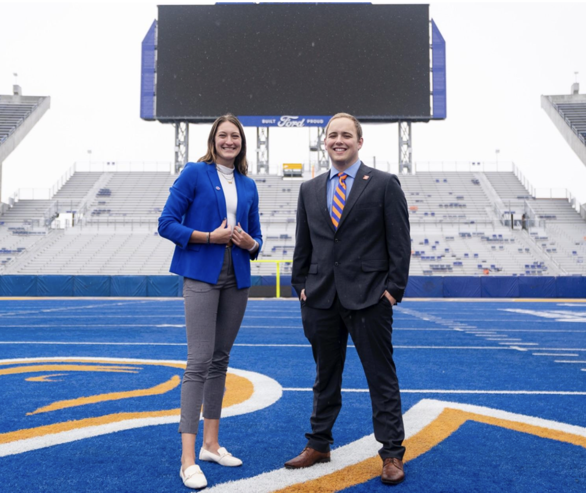 Two students standing on the blue turf field side by side