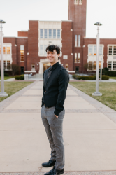 Student smiling standing in front of brick building with hands in pocket