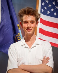 Caden Skelton standing in front of two flags