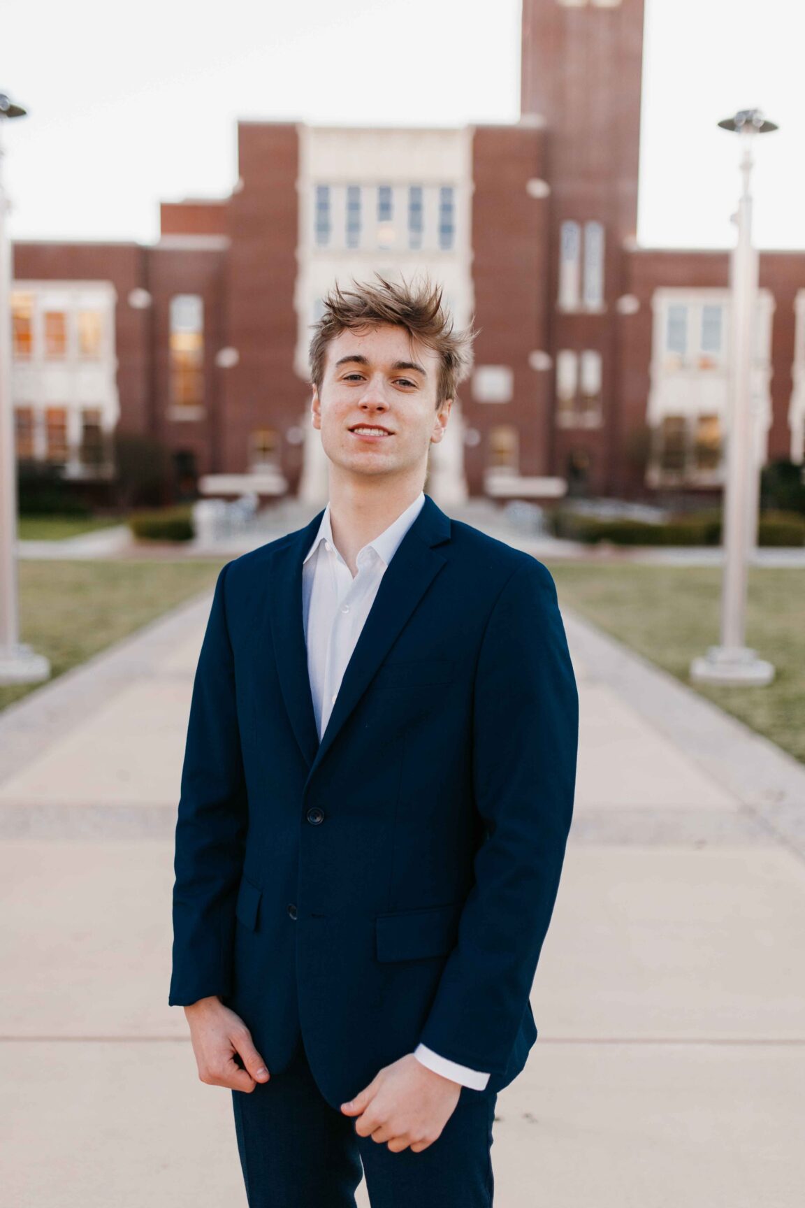 Gavin Manning stands in front of a brick building smiling