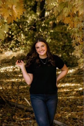 Annika Williams standing in front of autumn trees smiling