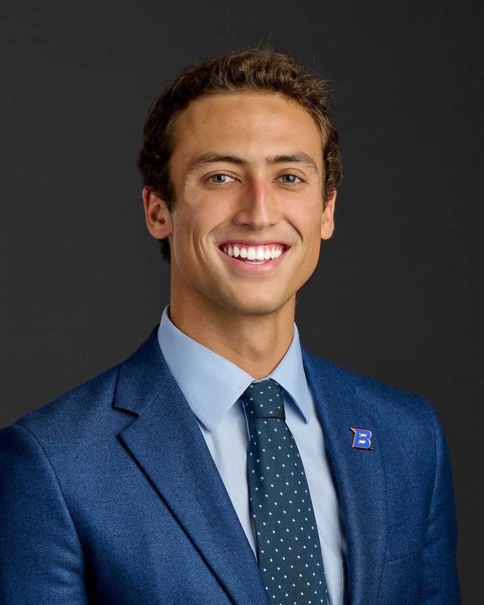 Sean Masi wearing a navy blue suit smiling against black background