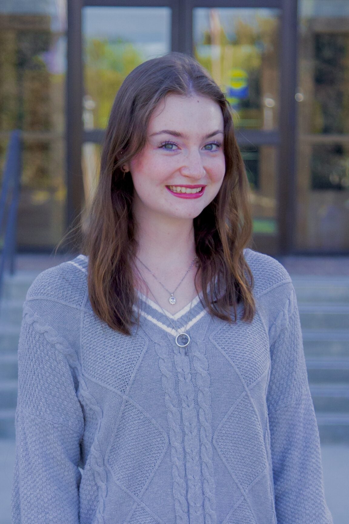 Alexis Gessler stands in front of glass doors, smiling