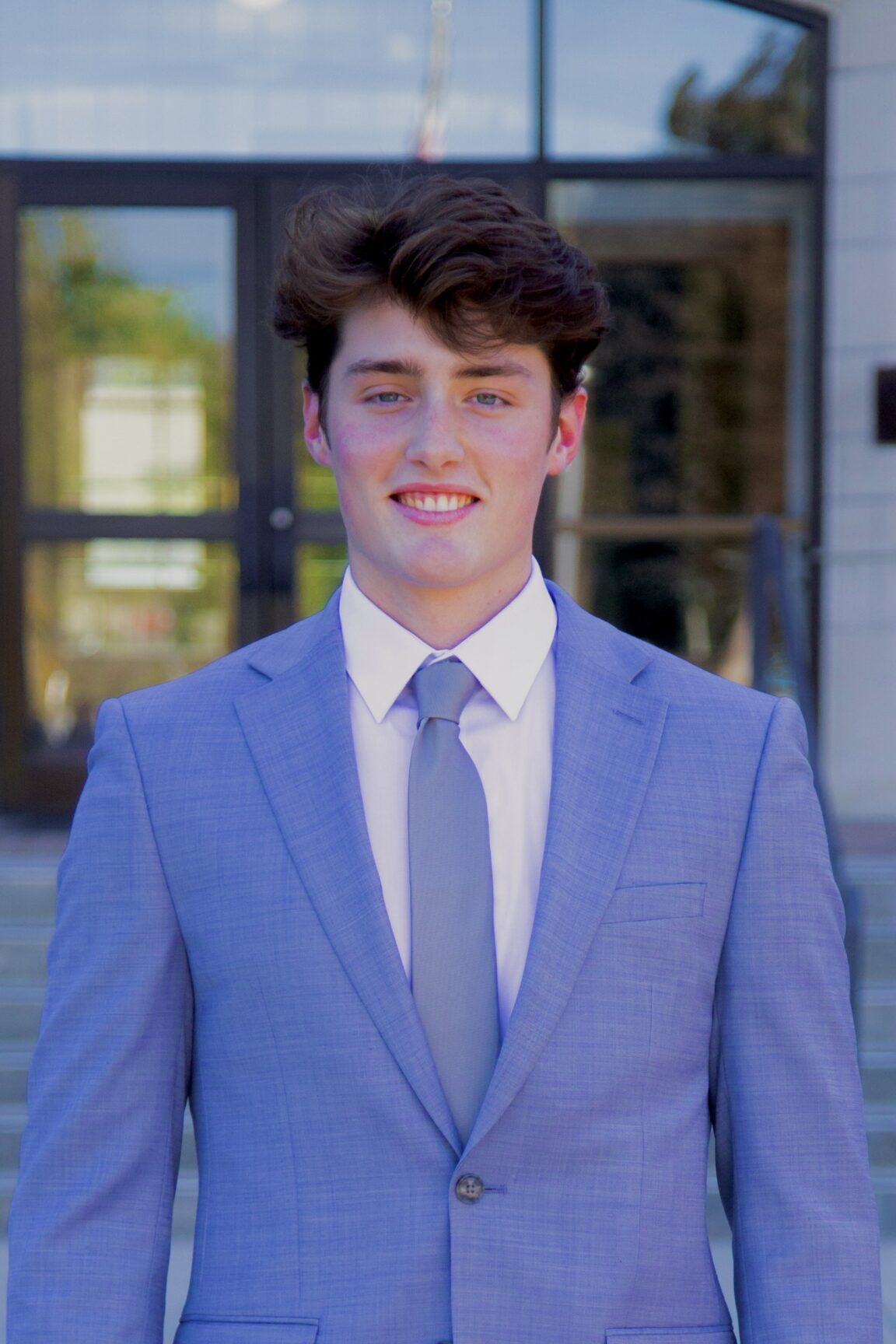 Cole Rebello stands in front of glass doors, smiling