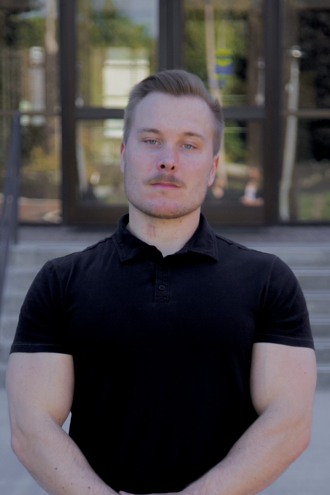 Jeremy Naftzger stands in front of glass doors with a serious expression