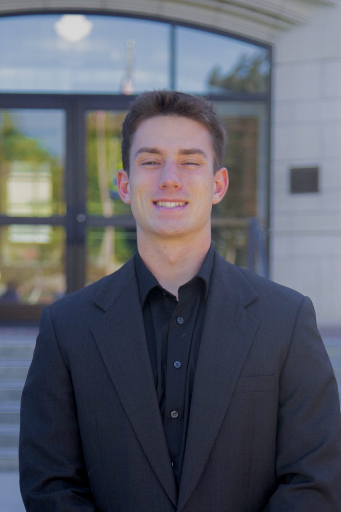 Roman Messina stands in front of glass doors, smiling