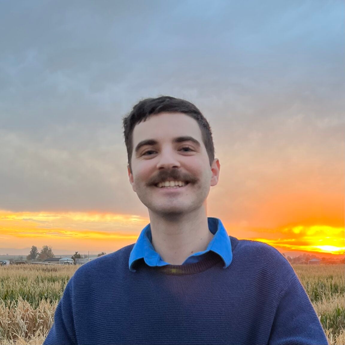 David Bru stands in front of a yellow-orange sunset, smiling