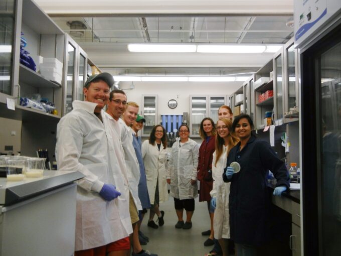 10 researchers in lab coats pose for photo in lab