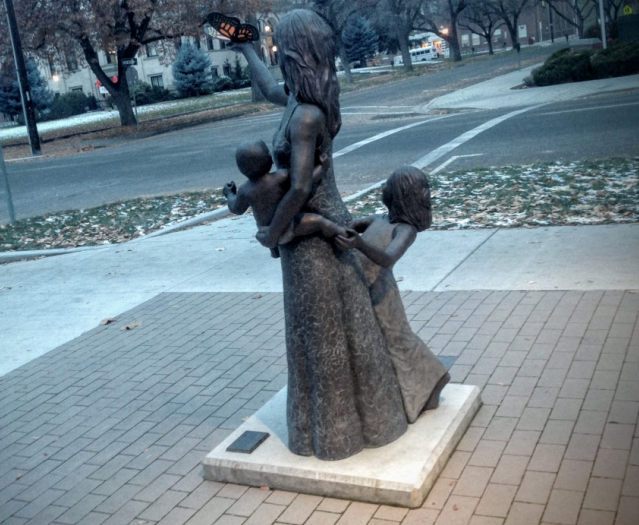 Statue of Mother holding infant with young girl standing next to her, mother holds butterfly in her hand as it is ready to fly