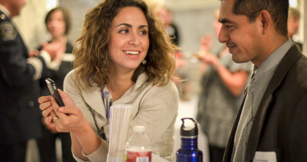 Two people conversing at a table while one of them holds up a phone