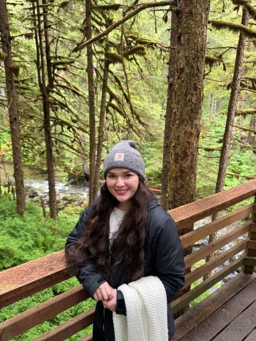 Photo of Maddie standing on a wooden bridge with trees and a river in the background