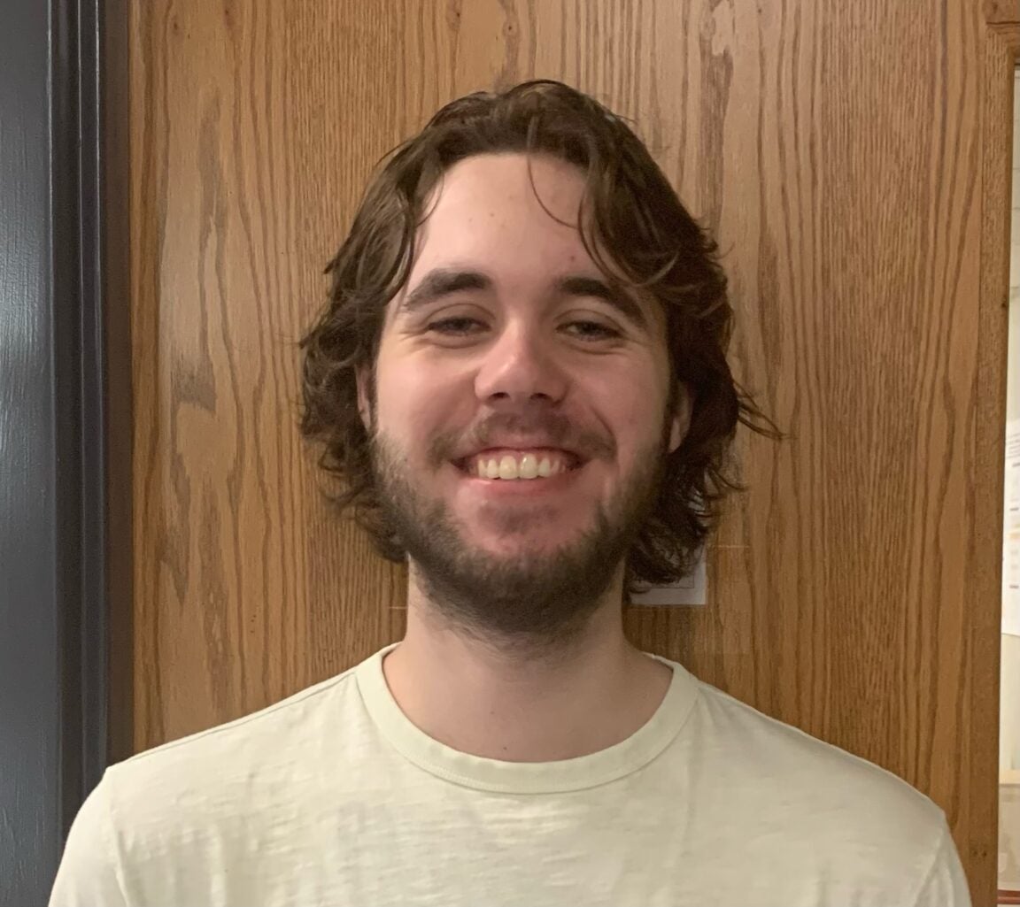 Photo of Marley Abrew standing in front of a wooden door