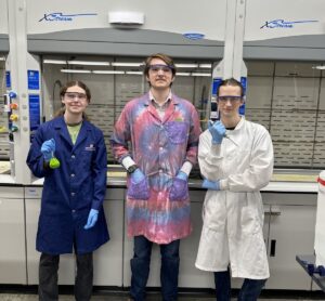 3 Project SEED students wearing lab coats and googles standing in a lab