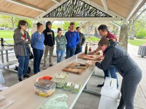 Photo of students gathered around a picnic table watching Oliviero Andreussi make a pizza