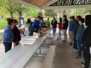 Photo of students gathered around a picnic table watching Oliviero Andreussi make a pizza