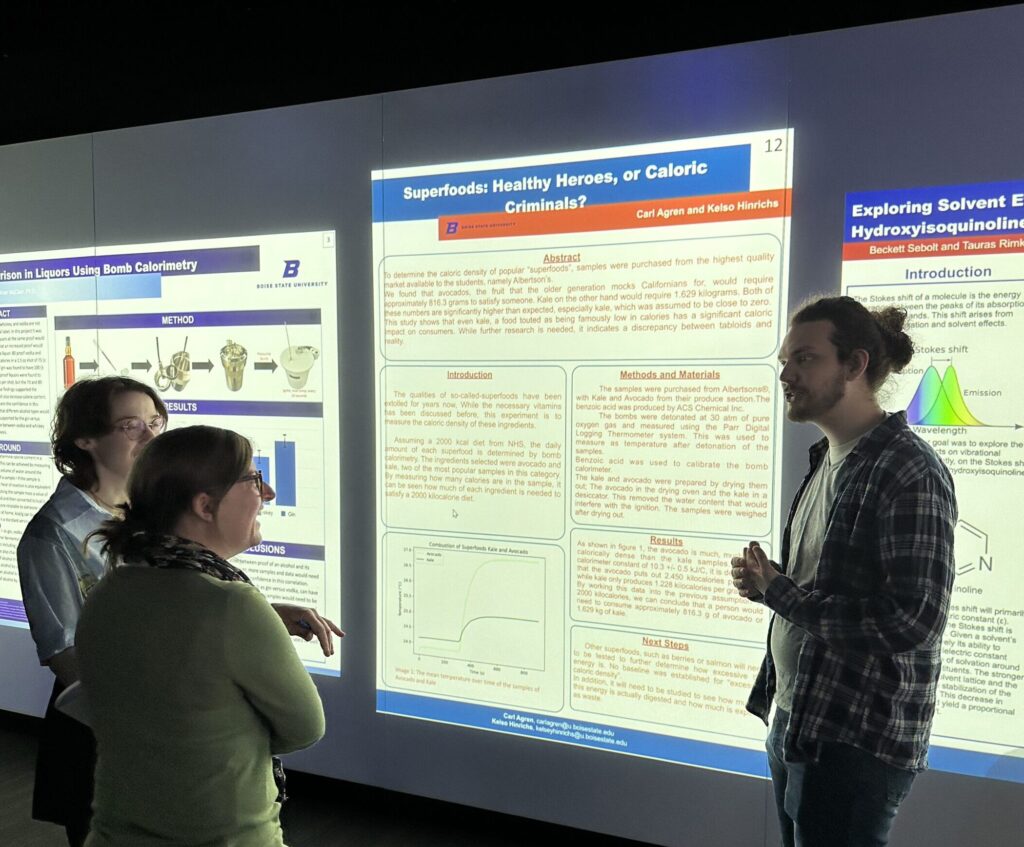 Photo of Carl Agren and Kelso Hinrichs explaining their PChem poster to Jenee Cyran