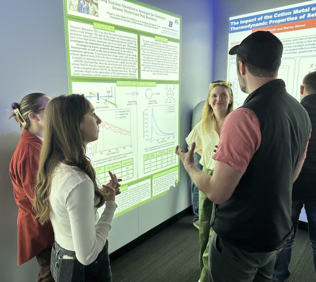 Photo of Lindsey Jenkins, Erykah Foss and Luca Manning explaining their PChem poster to Konrad Meister