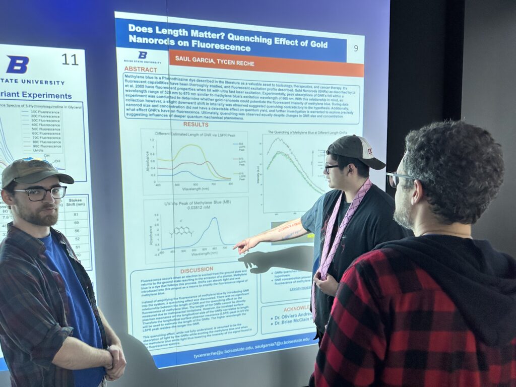 Photo of Saul Garcia and Tycen Reche explaining their PChem poster to Oliviero Andreussi