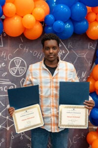 Photo of Hassan Mohamed holding two award certificates