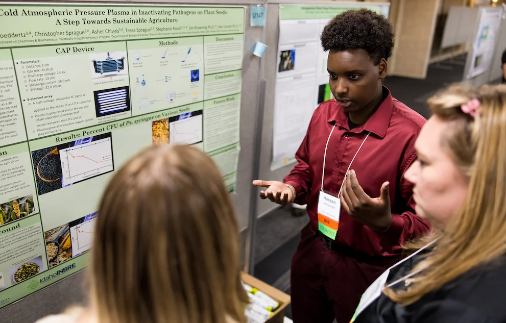 Photo of Hassan Mohamed in a red shirt explaining his poster at the INBRE State Conference