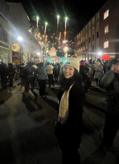 Photo of Hannah Dupay standing outside at night on a crowded street with fireworks in the background