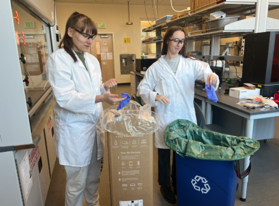 A photo of Lila Towers and Luca Manning in a lab sorting disposable gloves to place in a recycling bin