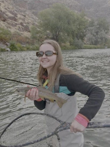 Photo of Tessa Sprague standing outside in a river, holding a net and a fish