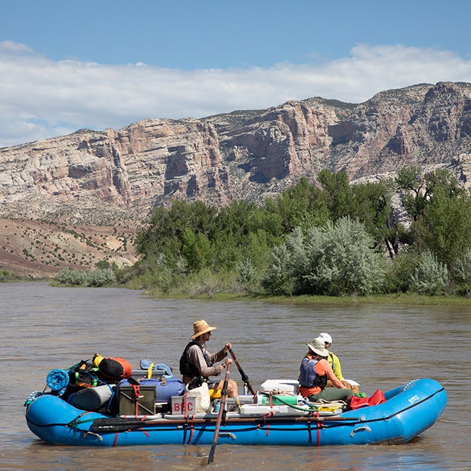 People paddle a raft down a muddy river in the American West