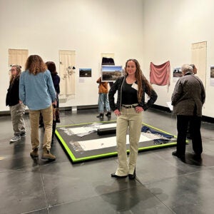 Lily Lee standing in front of her textile works in the gallery at the Tacoma Art Museum as part of the Soft Power exhibition