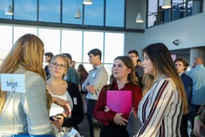 A group of three women in business casual dress talk to a representative standing beside a Simplot sign in a room with floor-to-ceiling windows.