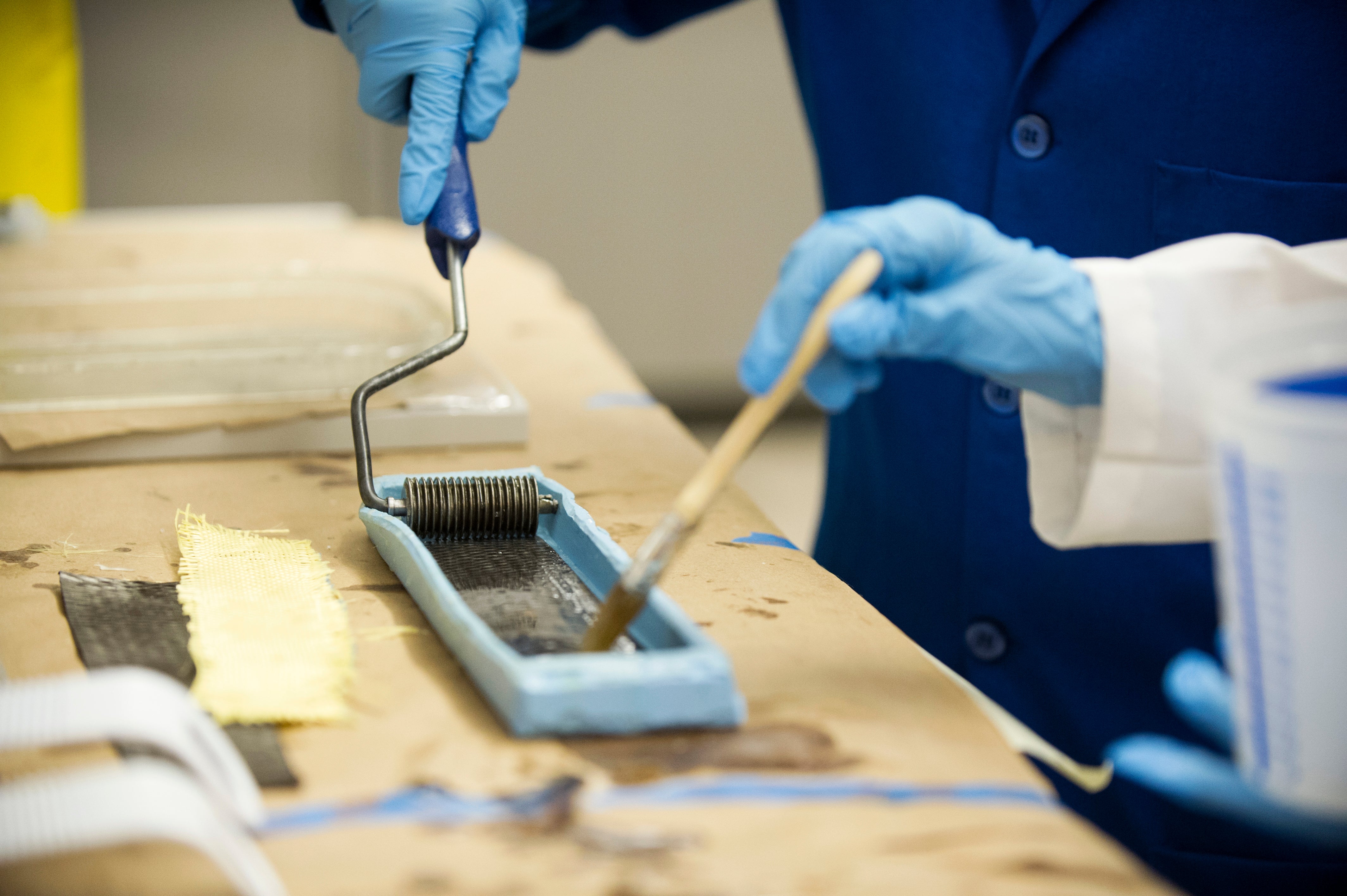 researcher rolls a grooved roller through a dark substance for an experiment in the Computational Materials Engineering Lab