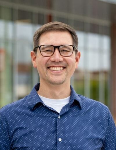 Portrait of Dr. Eric Jankowski wearing glasses and a blue shift