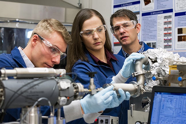 three individuals wearing safety equipment look over a vacuum chamber