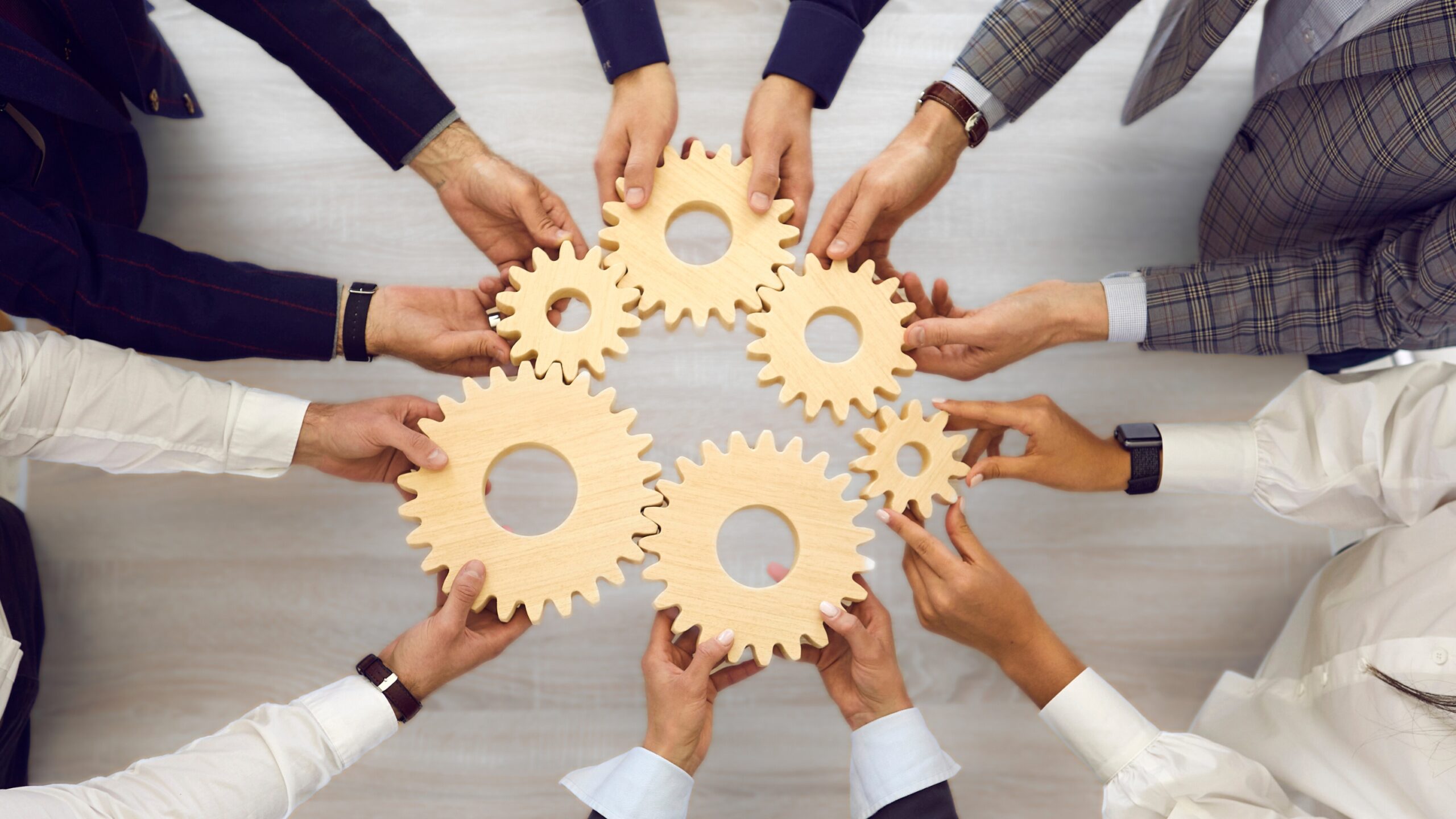 We see a group of people holding gears in their hands, symbolizing that by working together, the gears move and function well.