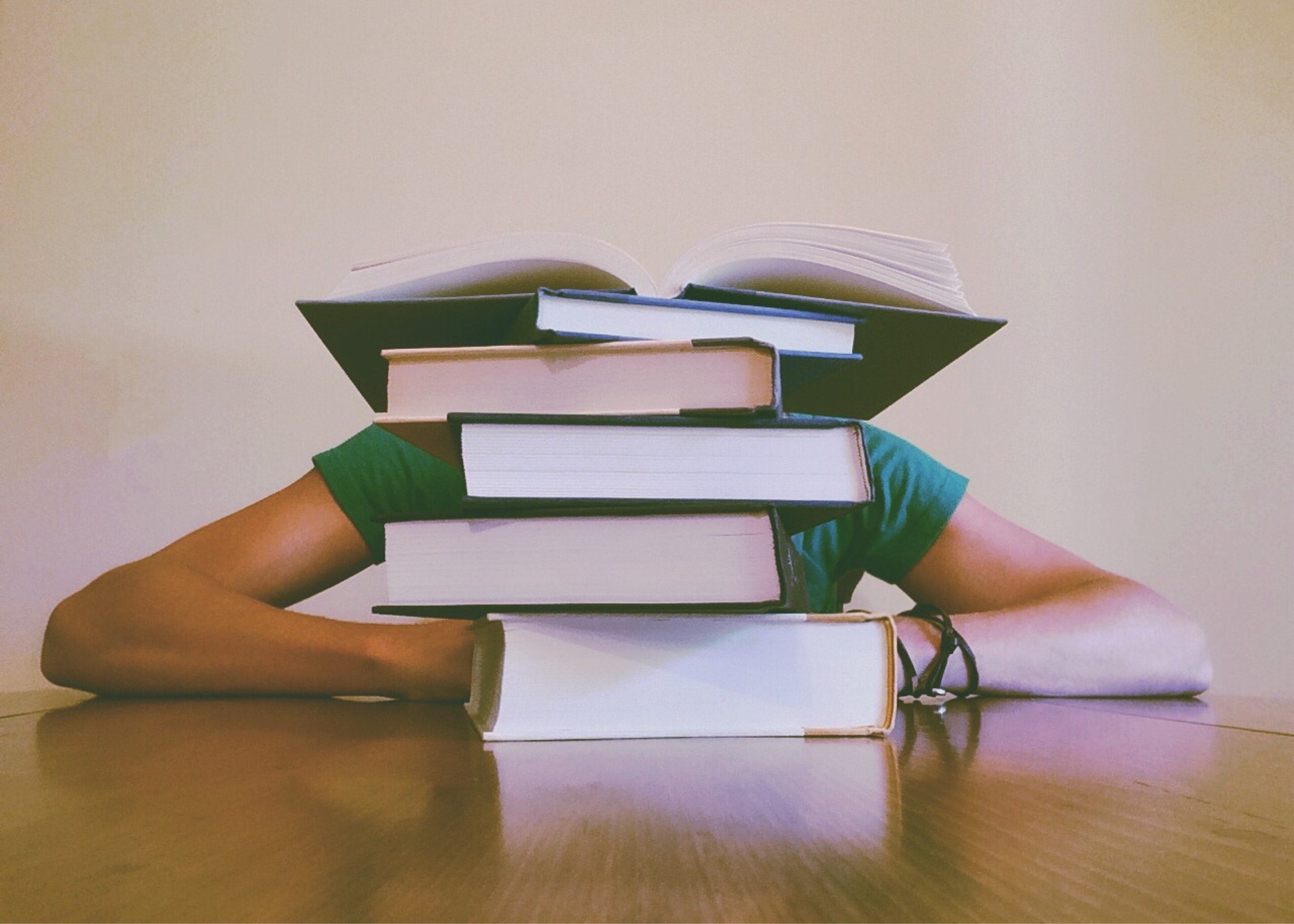 Student buried behind a pile of books. Photo by Pixabay from Pexels)