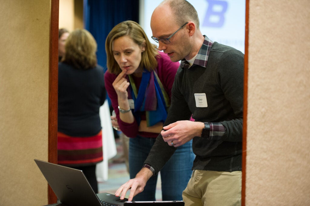 Two people stand together and look at a laptop.