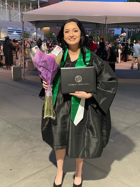 Sophia Guevara in a graduation gown holding flowers and degree certificate