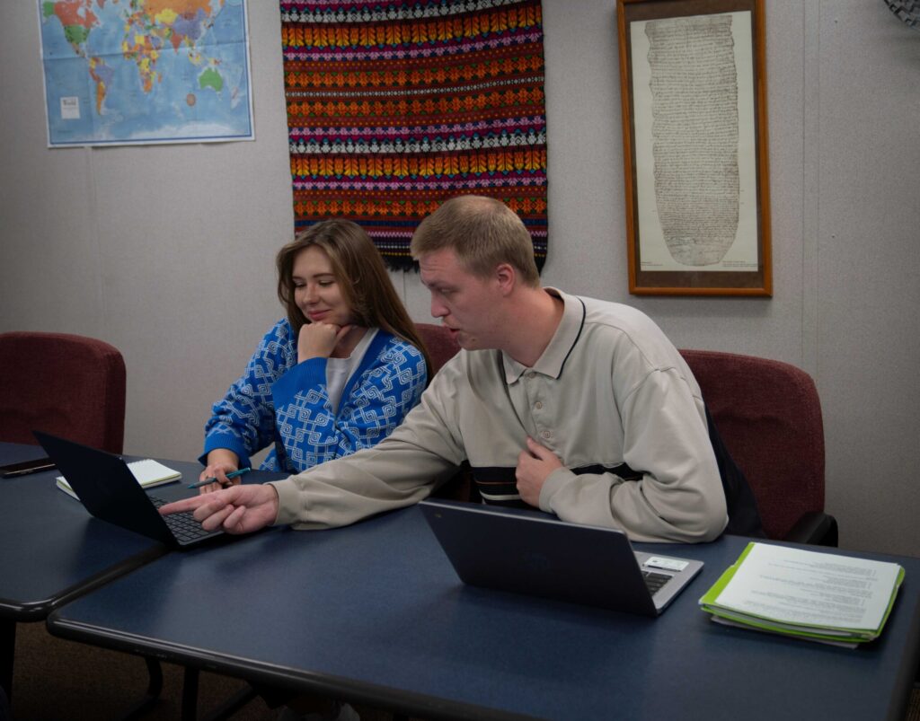 Two peers students looking at something on laptop screen while seated.