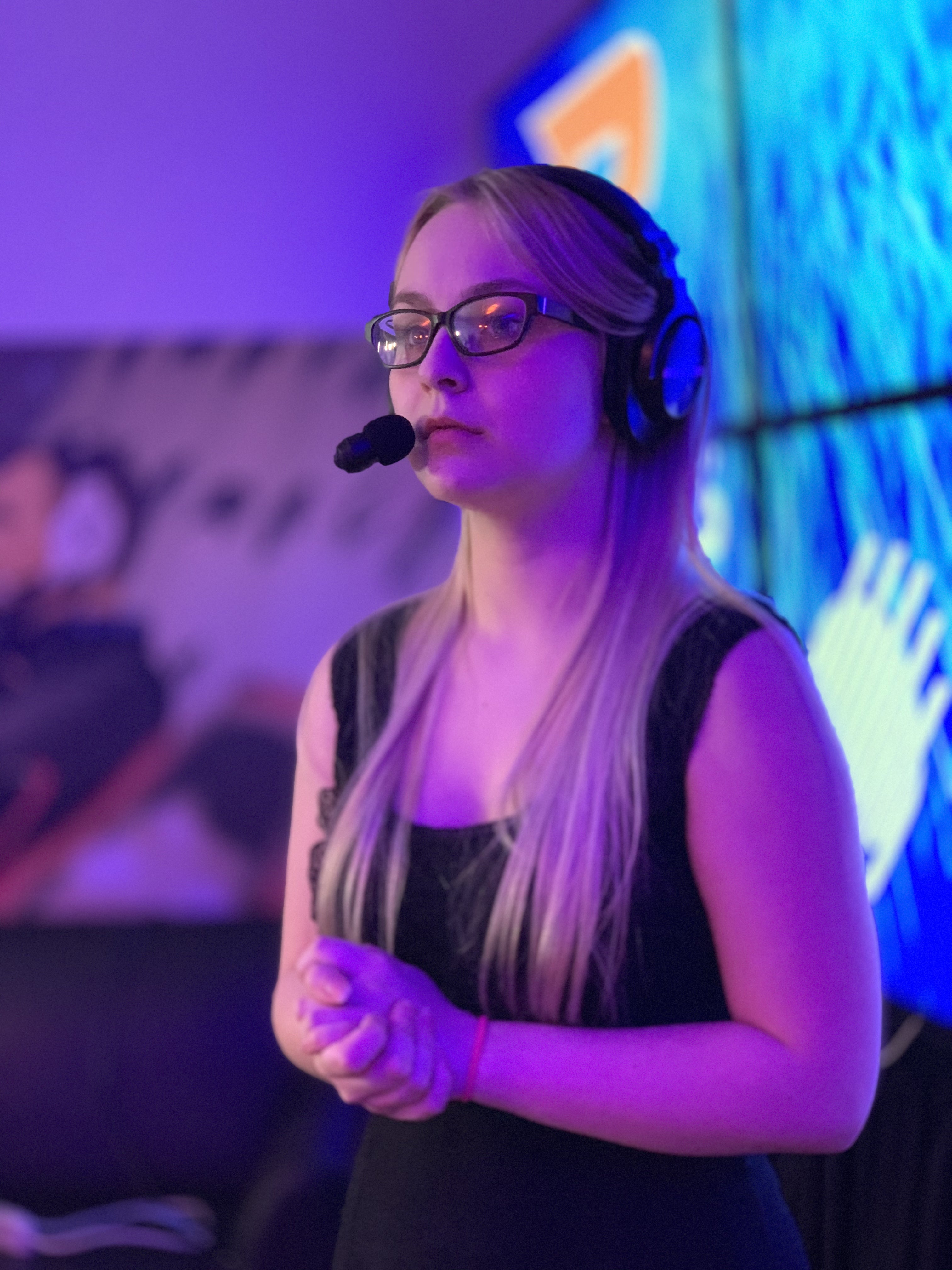 Female esports player with a headset and mic on in a pink lit room