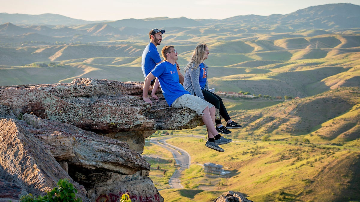 Three people sit on a rock overlooking the Boise foothills